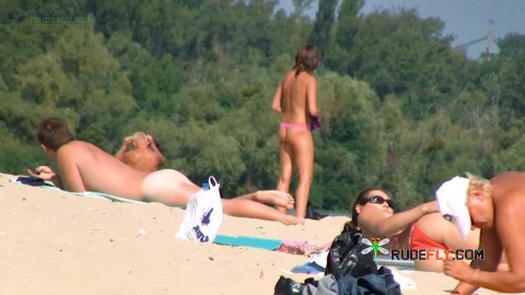 Nude beach girl sunbathes next to her man outdoors
